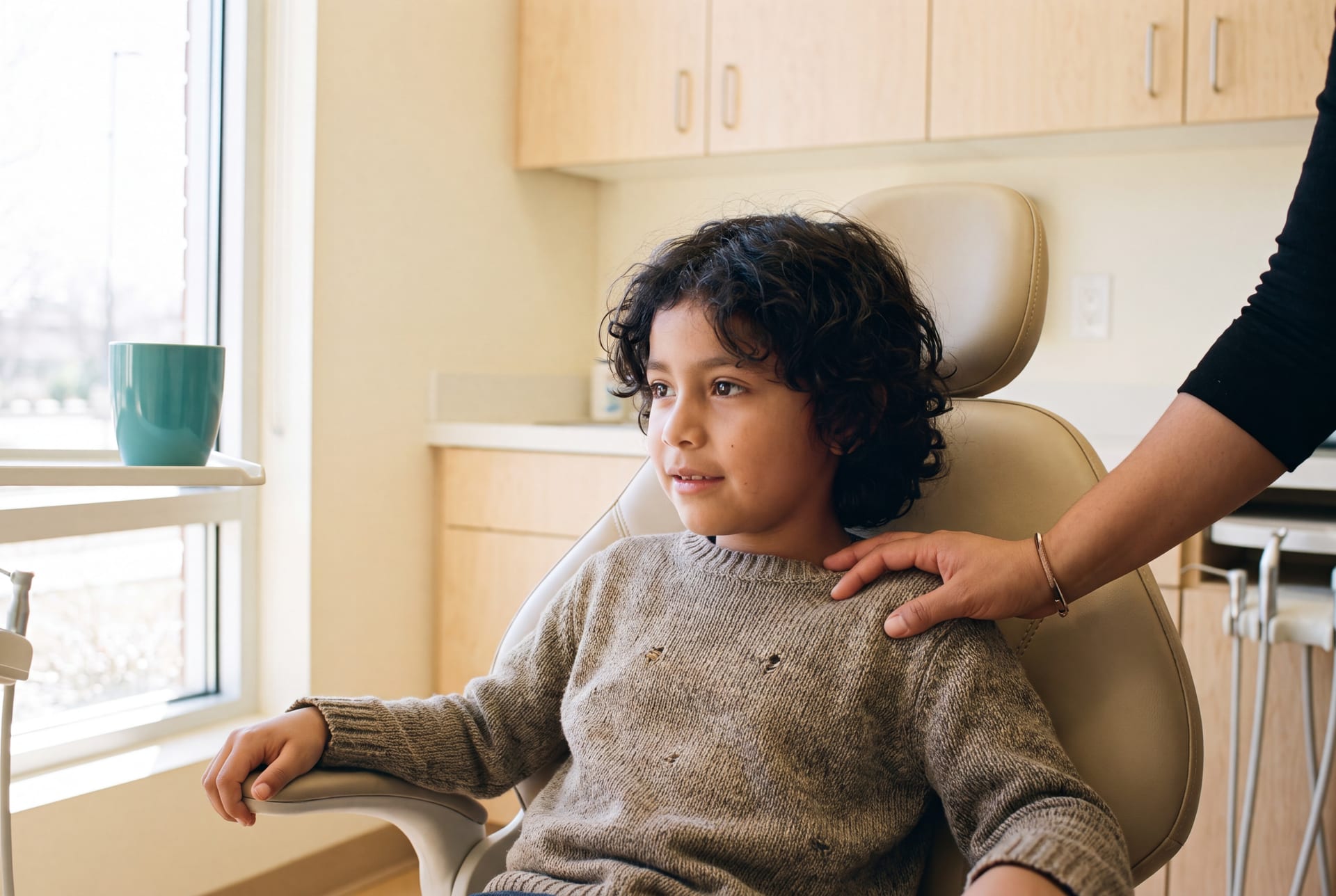 Niño tranquilo sentado en un sillón dental, acompañado por la mano de un adulto en su hombro